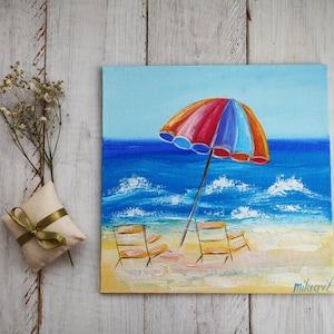 May include: A painting of a beach scene with two yellow chairs under a colorful striped beach umbrella. The ocean is blue with white waves and the sand is yellow. The painting is signed "Milaavet".