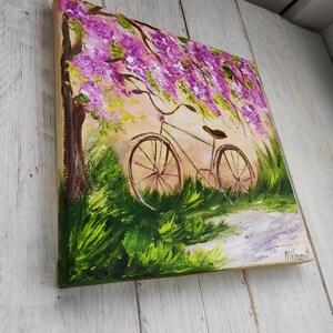 May include: A painting of a bicycle parked under a tree with purple flowers. The bicycle is brown with a white seat and has a basket on the handlebars. The background is a light green and yellow.