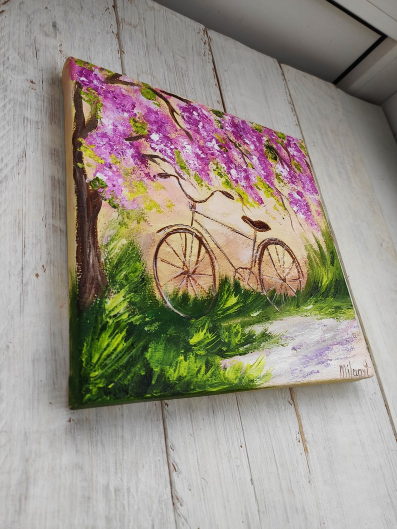 May include: A painting of a bicycle parked under a tree with purple flowers. The bicycle is brown with a white seat and has a basket on the handlebars. The background is a light green and yellow.