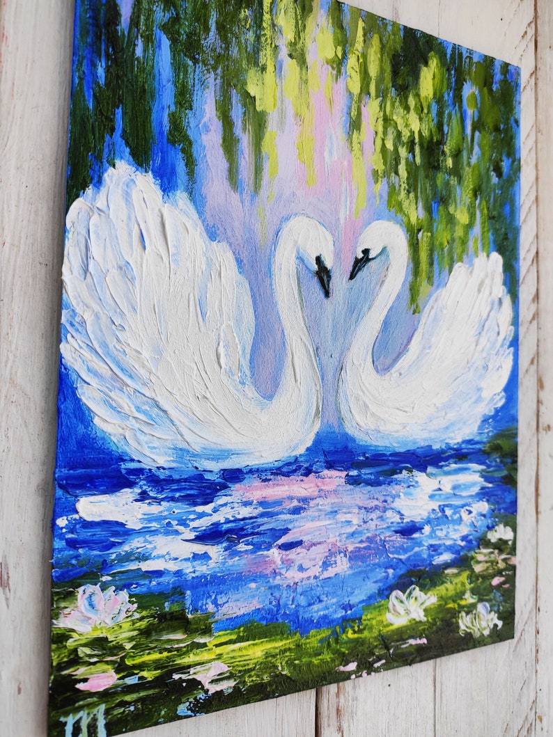 May include: A painting of two white swans with their necks intertwined, facing each other. The swans are in a blue lake with green lily pads and pink flowers. The background is a blue sky with green trees.