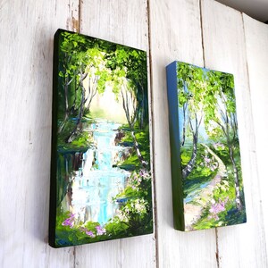 Op de afbeelding: Twee ingelijste schilderijen die natuursc&egrave;nes uitbeelden. Het schilderij aan de linkerkant toont een waterval in een groen bos. Het schilderij aan de rechterkant toont een pad door een berkenbos.