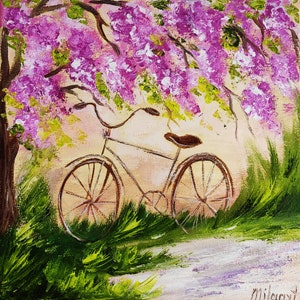 May include: A vintage bicycle with brown wheels is parked under a tree with pink blossoms. The bicycle is surrounded by green grass and a white path.