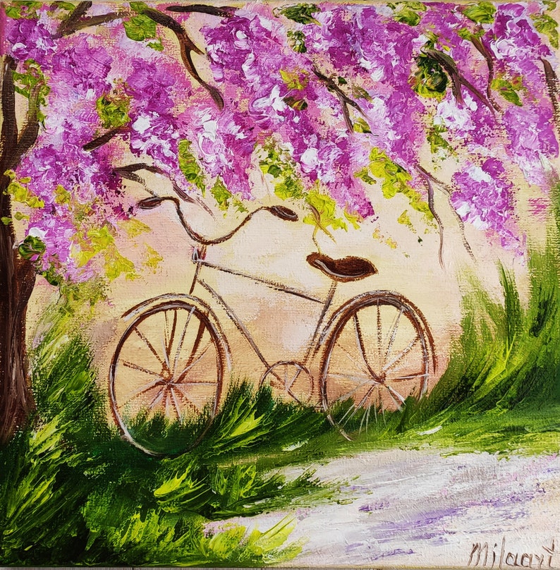 May include: A vintage bicycle with brown wheels is parked under a tree with pink blossoms. The bicycle is surrounded by green grass and a white path.