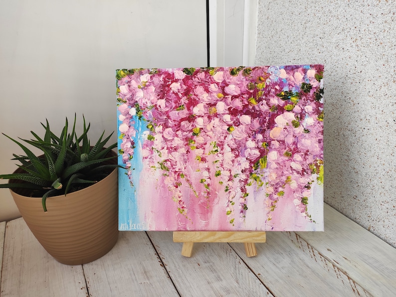 K&ouml;nnte beinhalten: Ein Gem&auml;lde auf Leinwand mit rosa und wei&szlig;en Blumen und gr&uuml;nen Bl&auml;ttern. Das Gem&auml;lde steht auf einem kleinen Staffelei.