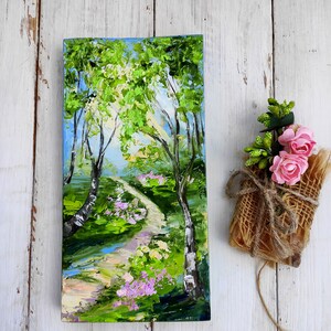 Op de afbeelding: Een schilderij van een pad dat door een groen bos slingert, met een blauwe lucht en witte wolken op de achtergrond. Het pad wordt geflankeerd door bomen en bloemen.
