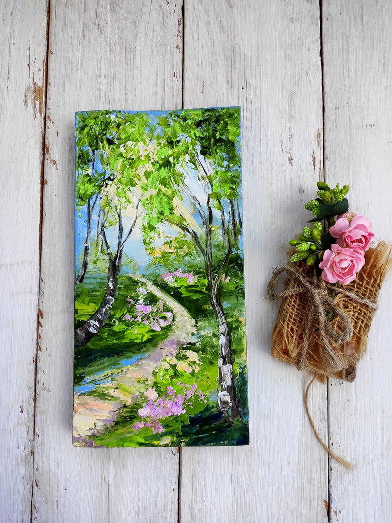 Op de afbeelding: Een schilderij van een pad dat door een groen bos slingert, met een blauwe lucht en witte wolken op de achtergrond. Het pad wordt geflankeerd door bomen en bloemen.