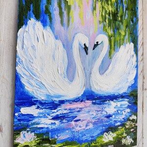 May include: A painting of two white swans with their necks intertwined, facing each other. The swans are in a blue lake with green lily pads and pink flowers. The background is a blue sky with green trees.