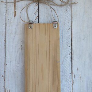 Op de afbeelding: Een leeg houten bord met een natuurlijke houten afwerking. Het bord hangt aan een touwtje met metalen haken aan de bovenkant.