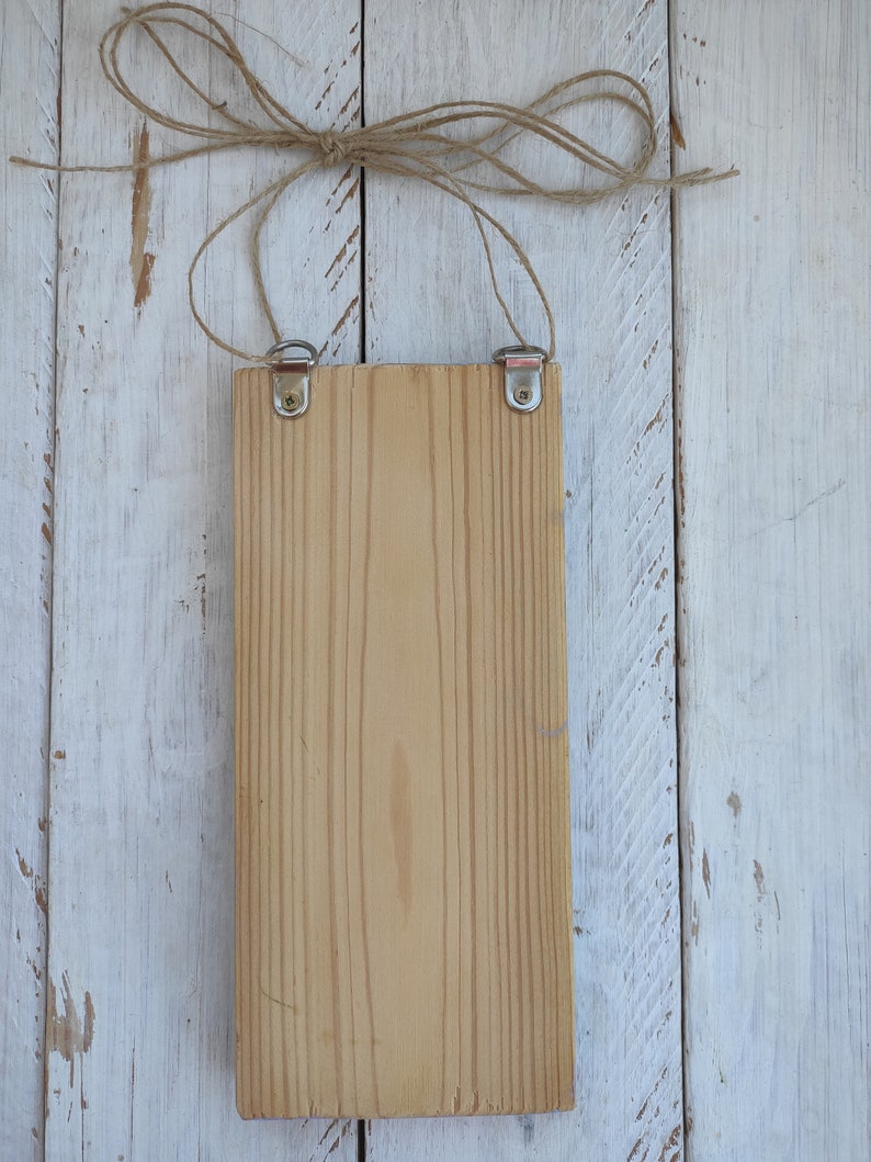 Op de afbeelding: Een leeg houten bord met een natuurlijke houten afwerking. Het bord hangt aan een touwtje met metalen haken aan de bovenkant.