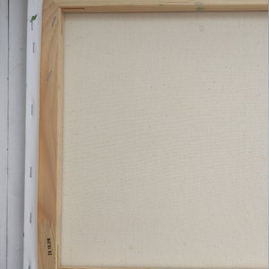 May include: The back of a stretched canvas with a wooden frame. The canvas is white and the frame is made of natural wood. The frame has a label with the number "11 11 23" printed on it.