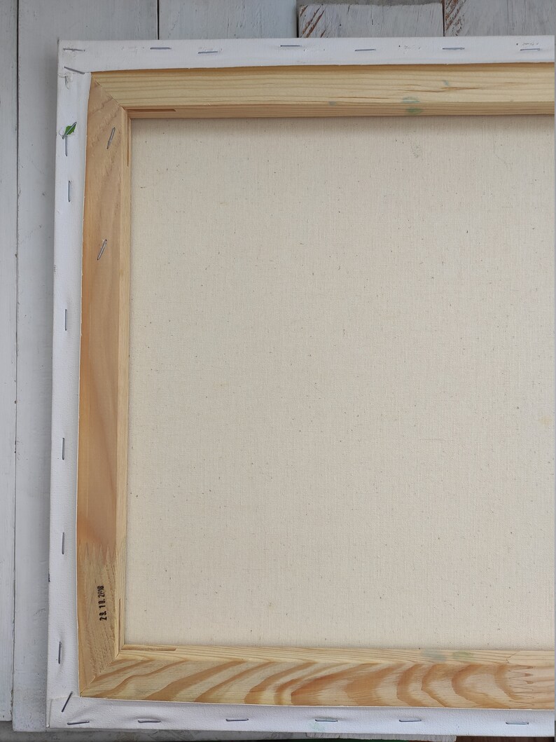 May include: The back of a stretched canvas with a wooden frame. The canvas is white and the frame is made of natural wood. The frame has a label with the number "11 11 23" printed on it.