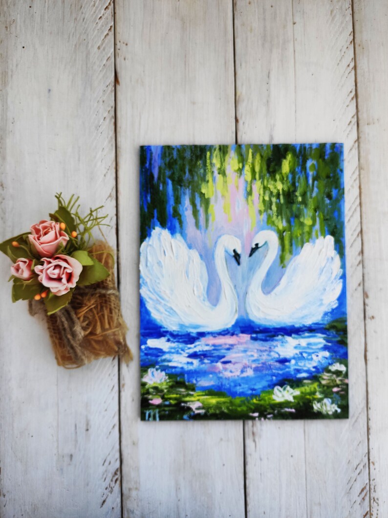 May include: A painting of two white swans with their necks intertwined, set against a backdrop of a blue lake with green foliage and lily pads. The swans are painted in a realistic style with visible brushstrokes.