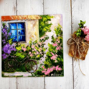 Könnte beinhalten: Ein Gemälde, das ein Haus mit einem blauen Fenster und einem Fahrrad davor zeigt. Das Haus ist von Blumen und Grün umgeben. Das Gemälde ist mit "milaart" signiert.