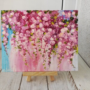 K&ouml;nnte beinhalten: Ein Gem&auml;lde mit rosa und lila Bl&uuml;ten mit gr&uuml;nen Bl&auml;ttern auf einem blauen und rosa Hintergrund. Das Gem&auml;lde steht auf einem kleinen Holzstaffelei.