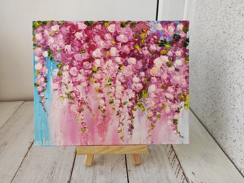 K&ouml;nnte beinhalten: Ein Gem&auml;lde mit rosa und lila Bl&uuml;ten mit gr&uuml;nen Bl&auml;ttern auf einem blauen und rosa Hintergrund. Das Gem&auml;lde steht auf einem kleinen Holzstaffelei.