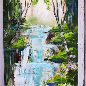 Op de afbeelding: Een schilderij van een waterval in een bos. Het water is helderblauw en wit, en de bomen zijn groen. Op de voorgrond zijn roze bloemen te zien.