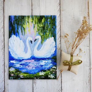 May include: A painting of two white swans with their necks intertwined, facing each other. The swans are in a blue pond with green lily pads and white flowers. The background is a green and blue forest.