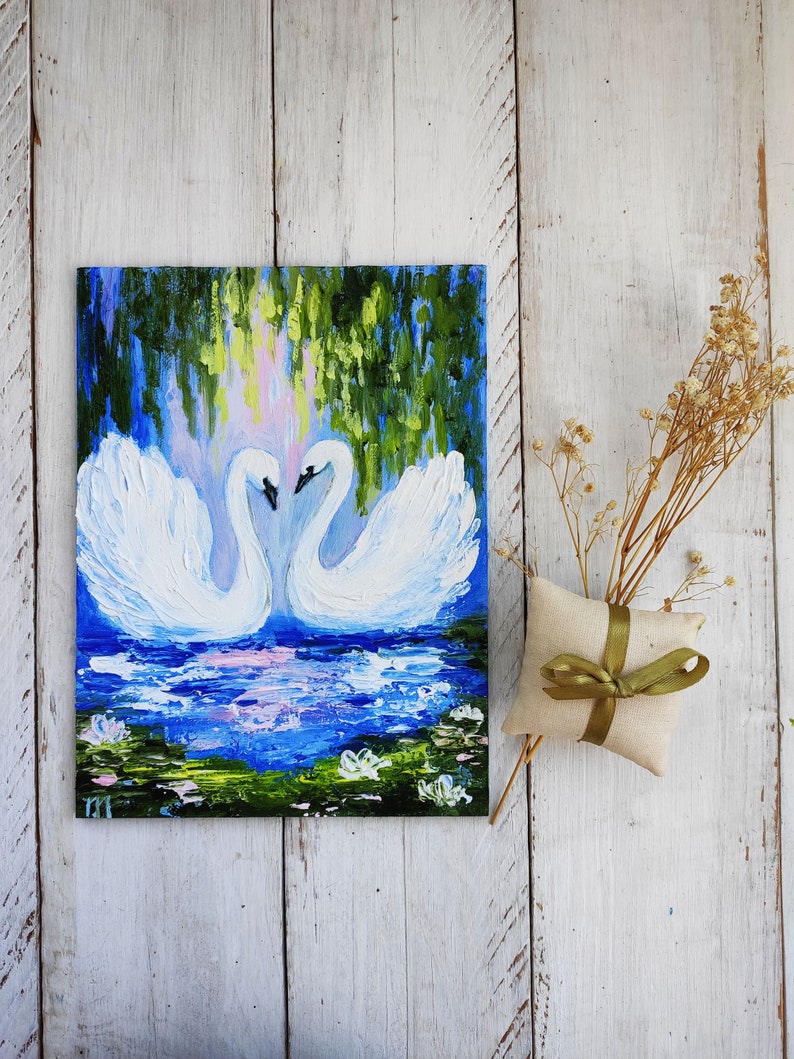 May include: A painting of two white swans with their necks intertwined, facing each other. The swans are in a blue pond with green lily pads and white flowers. The background is a green and blue forest.
