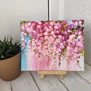K&ouml;nnte beinhalten: Ein Gem&auml;lde auf Leinwand mit rosa und wei&szlig;en Blumen und gr&uuml;nen Bl&auml;ttern. Das Gem&auml;lde steht auf einem kleinen Staffelei.