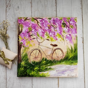May include: A painting of a bicycle parked under a tree with pink flowers. The bicycle is brown with a white seat and has a basket on the handlebars. The background is a light blue sky with white clouds.