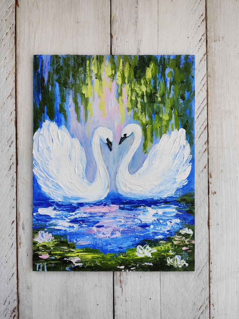 May include: A painting of two white swans with their necks intertwined, facing each other. The swans are in a blue pond with green lily pads and white flowers. The background is a blue sky with green trees.