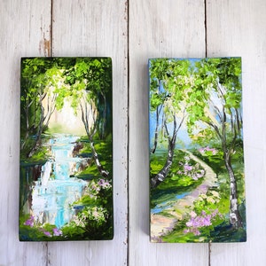 Op de afbeelding: Twee kleine schilderijen op canvas, die elk een andere sc&egrave;ne in een bos voorstellen. Het schilderij links toont een waterval in een groen bos met een blauwe lucht erboven. Het schilderij rechts toont een pad dat door een groen bos slingert met een blauwe lucht erboven.