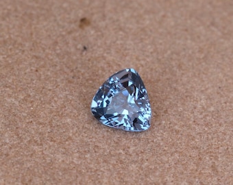 Pode incluir: Uma gema triangular azul claro com facetas, sobre um fundo marrom.