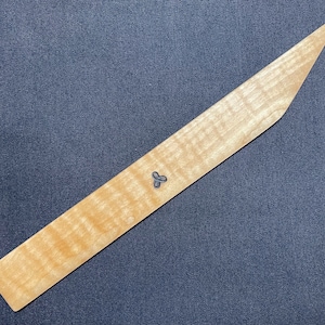 May include: A long, thin, wooden ruler with a pointed end and a small, three-leaf clover design in the center. The ruler is made of light wood with a natural grain pattern.
