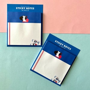 May include: Two packs of blue sticky notes with red and white illustrations of a rabbit and candy. The text on the packs reads "Sticky Notes 50 Sheets" and "Etaine Illustrate".
