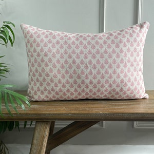 May include: A pink and white patterned lumbar cushion with a floral design. The cushion is sitting on a wooden bench.