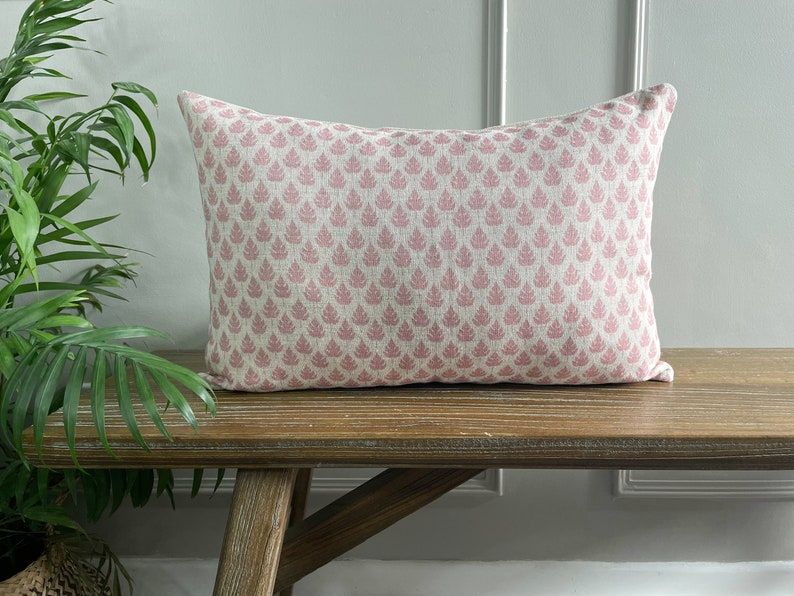 May include: A pink and white patterned lumbar cushion with a floral design. The cushion is sitting on a wooden bench.
