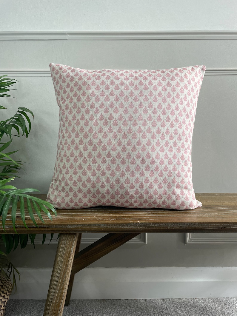 May include: A pink and white patterned cushion with a leaf design. The cushion is sitting on a wooden bench.
