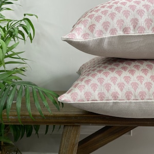 May include: Two pink and white patterned throw pillows with a leaf design are stacked on a wooden bench.
