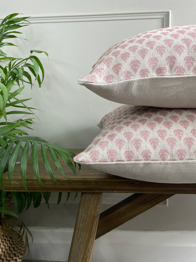 May include: Two pink and white patterned throw pillows with a leaf design are stacked on a wooden bench.