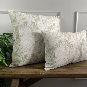 May include: Two decorative throw pillows with a fern pattern on a light beige background. The pillows are on a wooden bench.