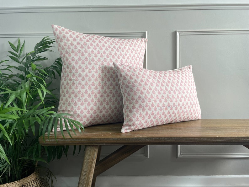 May include: Two pink and white patterned throw cushions on a wooden bench. The cushions have a floral design.