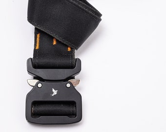 May include: A black nylon belt with an orange stitching detail and a black metal buckle. The buckle has a small silver lever and a logo of a bird.