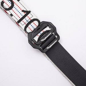 May include: A white and black patterned belt with a black buckle. The buckle has the word "Flybooster" printed on it.