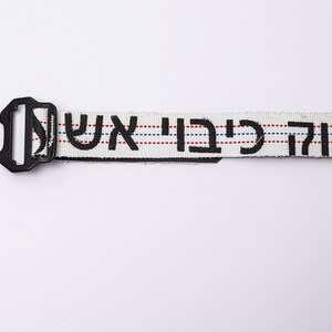 May include: White belt with black Hebrew lettering and red and blue stripes. The belt has a black plastic buckle.