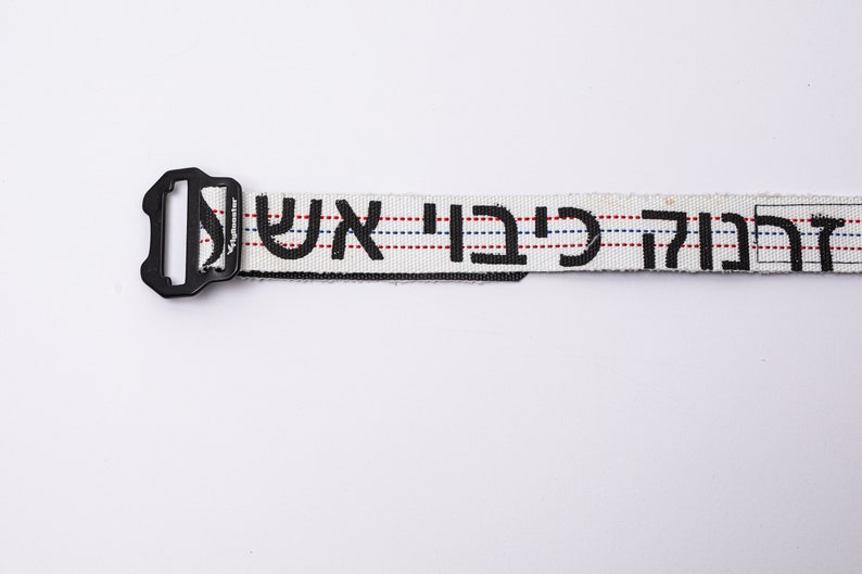 May include: White belt with black Hebrew lettering and red and blue stripes. The belt has a black plastic buckle.