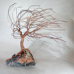 May include: A wire sculpture of a tree with copper and silver wire branches, set on a dark gray rock base.