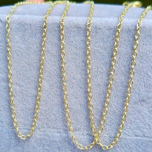 May include: Several delicate gold-colored chain necklaces with small, oval links are displayed against a soft, light blue background. The chains are draped, showcasing their length and design. The chains are likely for jewelry.
