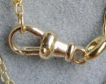 May include: Close-up of a gold-colored necklace chain with a lobster clasp. The chain is made of small, rectangular links. The clasp is a rounded shape with a lever to open and close. The background is a solid gray color.