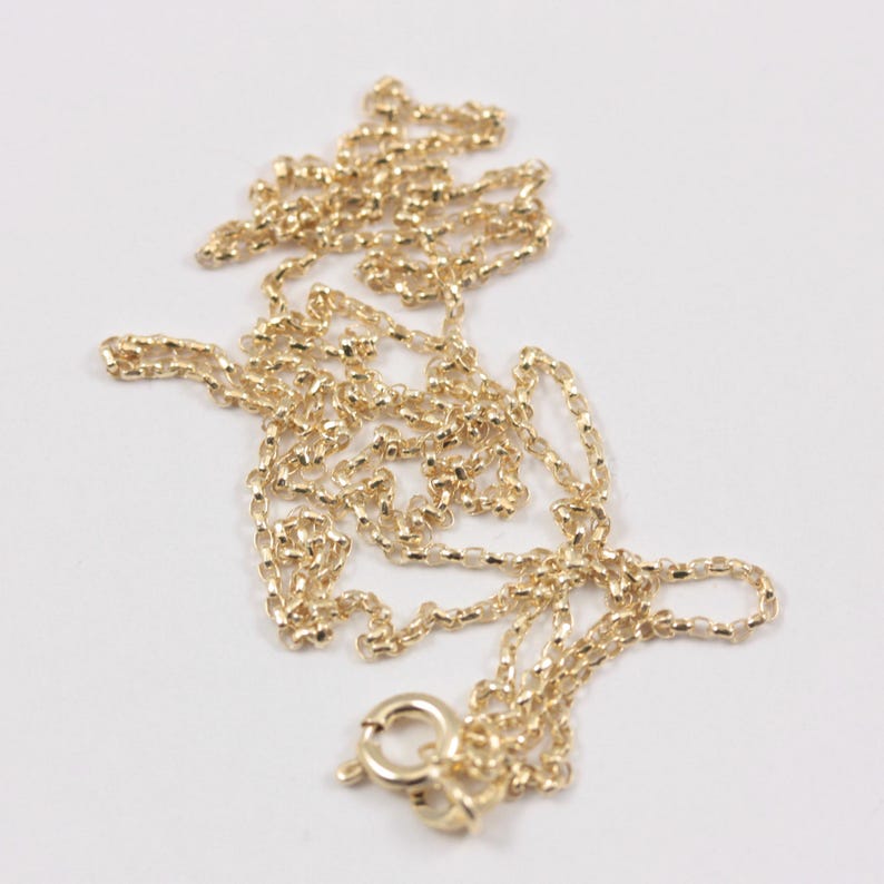 K&ouml;nnte beinhalten: Eine zarte, goldfarbene Halskette mit kleinem Verschluss. Die Kette besteht aus kleinen, verbundenen Gliedern, die ein strukturiertes Aussehen erzeugen. Die Halskette wird auf einer wei&szlig;en Oberfl&auml;che pr&auml;sentiert, um ihre Farbe und ihr Design hervorzuheben.