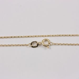 K&ouml;nnte beinhalten: Eine filigrane Goldkette mit einem Box-Chain-Design. Die Halskette hat einen Karabinerverschluss und ein kleines Etikett mit der Pr&auml;gung "375". Die Kette wird vor einem wei&szlig;en Hintergrund gezeigt.