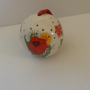 May include: White ceramic egg-shaped ornament with a red floral design. The ornament has a red string loop for hanging.