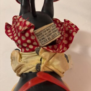 May include: Vintage Minnie Mouse figurine, with a black body, red shoes, and a red and white polka dot skirt. The figurine has a yellow top and red suspenders. A tag is attached to the back.