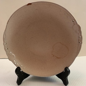 May include: A white ceramic plate with a scalloped edge and a textured surface. The plate is on a black stand.