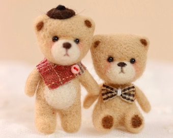 May include: Two small, brown felt teddy bears. The bear on the left is wearing a red and white plaid scarf and a black hat. The bear on the right is wearing a brown and white bow tie.
