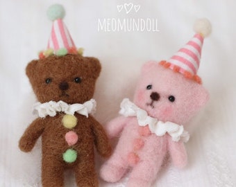 May include: Two small felt teddy bears wearing party hats. The bear on the left is brown with a yellow, pink, and green polka dot pattern on its chest. The bear on the right is pink with a pink polka dot pattern on its chest. Both bears have white ruffled collars.